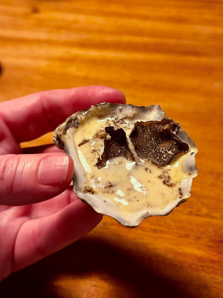 A customer holding one of the baked oysters with truffle cream sauce in his hand