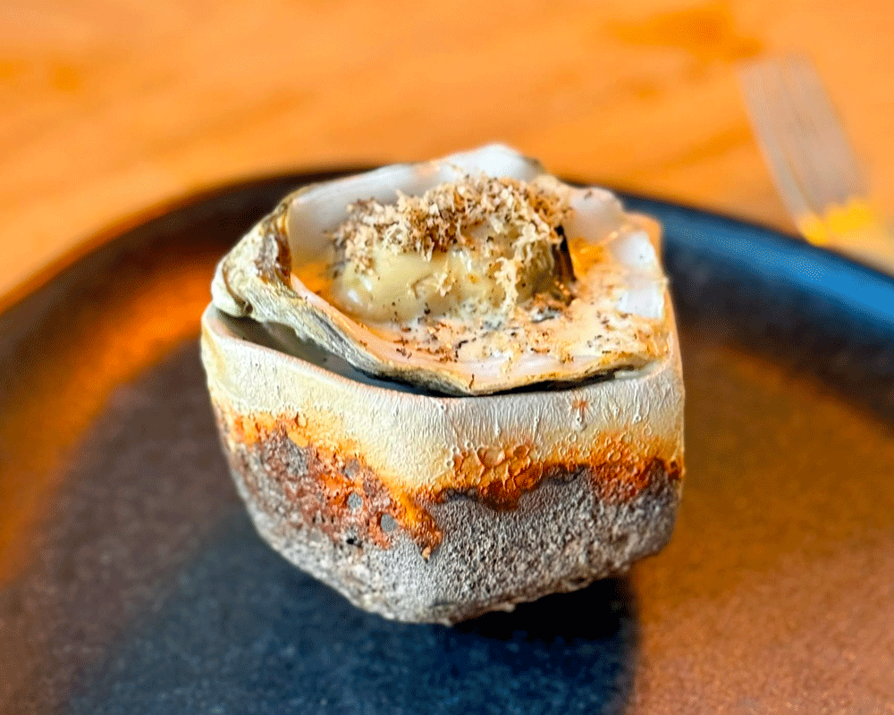 A plated baked oyster with truffle cream sauce